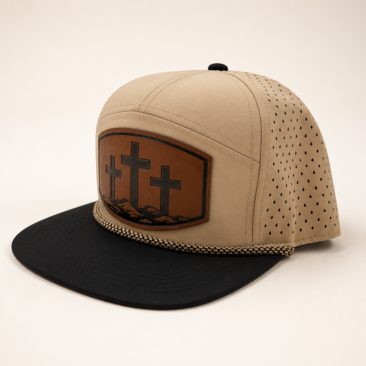 Tan and black Three Cross hat, angled view showing the patch, rope detail, and perforated side panels