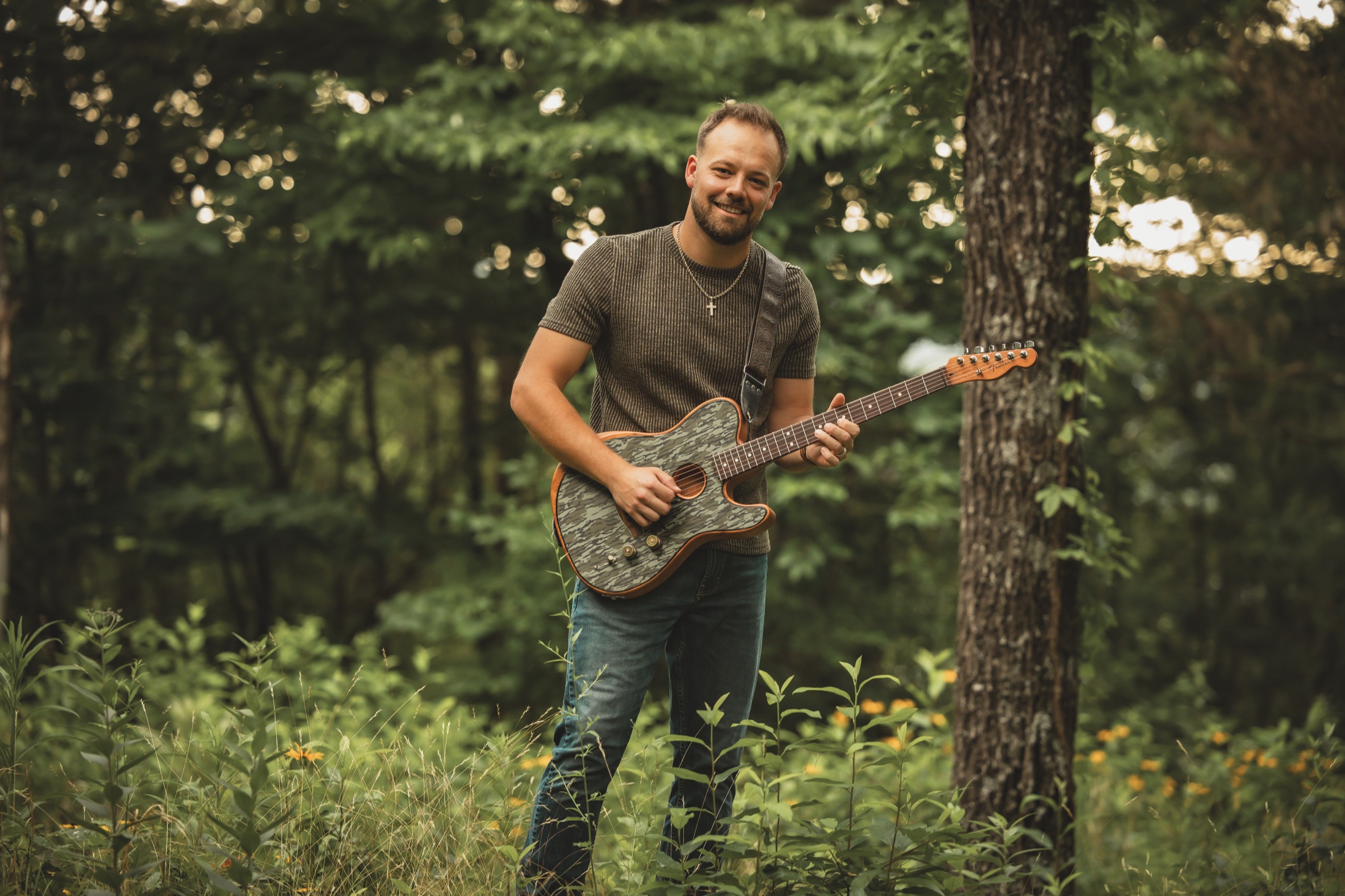 Dodge Andersen holding his guitar in the woods